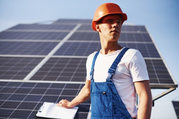 Con documentos. Trabajador de sexo masculino en uniforme azul al aire libre con baterías solares en un día soleado.