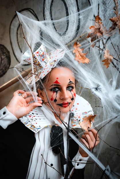 Doçura ou travessura. retrato de jovem com maquiagem assustadora, vestindo a fantasia de rainha de copas com colar de cartão, olhando para a câmera através da teia de aranha durante uma visita à noite da festa de halloween