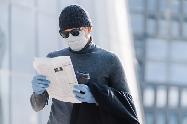 Doença da gripe, proteção contra a propagação de vírus. Jovem usa máscara médica contra vírus da gripe ou coronavírus, coloca no espaço público, lê a imprensa com olhar concentrado. Conceito de cuidados de saúde