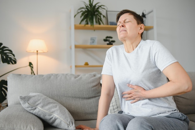 Foto doente chateada senhora de meia-idade segura barriga sofre de dor de abdômen conceito mulher adulta velha madura sente dor matinal dor no estômago gastrite abdominal pancreatite diarréia problema sintoma sente-se na cama