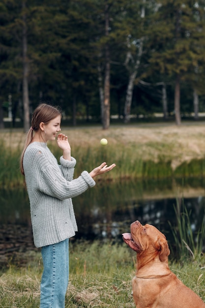 Dogue de Bordeaux ou Mastiff francês com jovem mulher brincando com bola no parque ao ar livre.