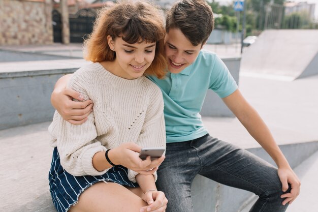 Dois adolescente, menino e menina no parque e usando o smartphone.