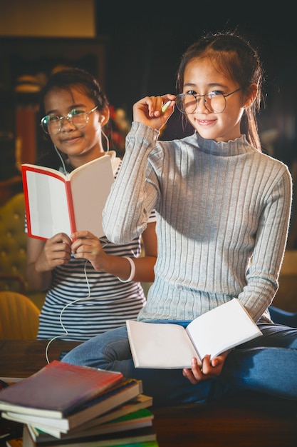 Dois adolescentes asiáticos e livreto na mão, sentado na biblioteca