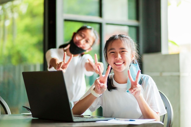 Foto dois adolescentes asiáticos sorrindo com cara de felicidade enquanto tiram a máscara facial de proteção