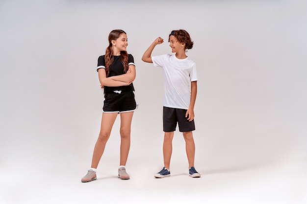 Dois adolescentes se exercitando juntos, garoto mostrando seus bíceps para uma linda garota, eles parados isolados