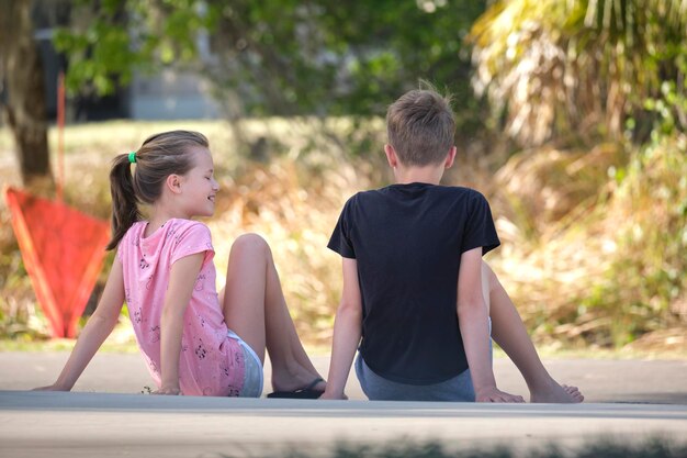 Dois adolescentes sorridentes felizes, menino e menina sentados ao ar livre descansando se divertindo no dia ensolarado de verão