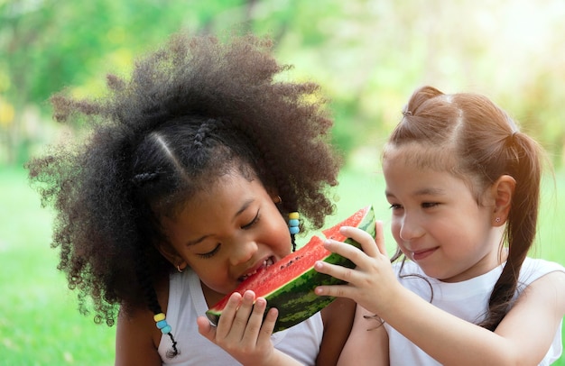 Foto dois adorável garotinha comendo melancia no parque num dia de verão.