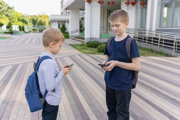 Dois alunos com mochilas em pé no fundo da escola e conversando ao telefone com cada um