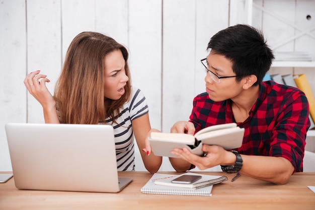 Dois alunos em um local de trabalho aprendendo com laptop e livros