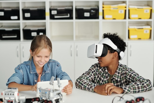 Dois alunos interculturais inteligentes jogando jogo virtual na aula de robótica