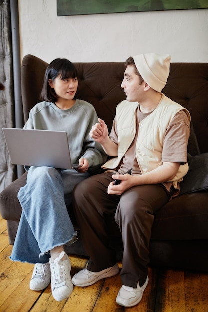 Dois alunos sentados no sofá usando um laptop e discutindo educação online juntos na sala