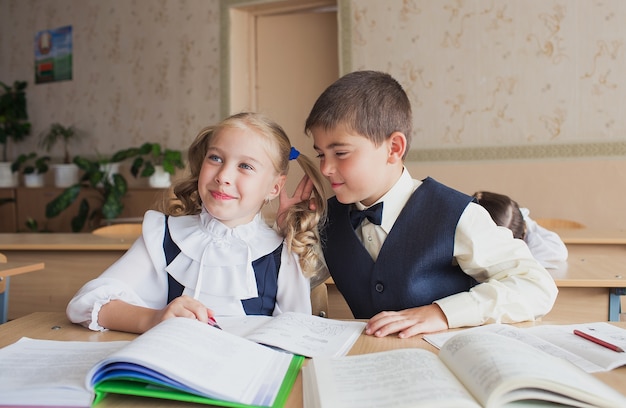 Dois alunos, um menino e uma menina, sentam-se em uma mesa na escola e se comunicam pelo ouvido