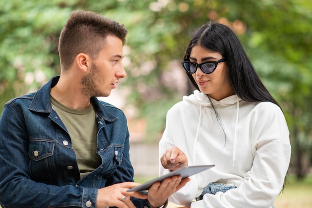 Dois alunos usando um tablet digital sentado em um banco ao ar livre