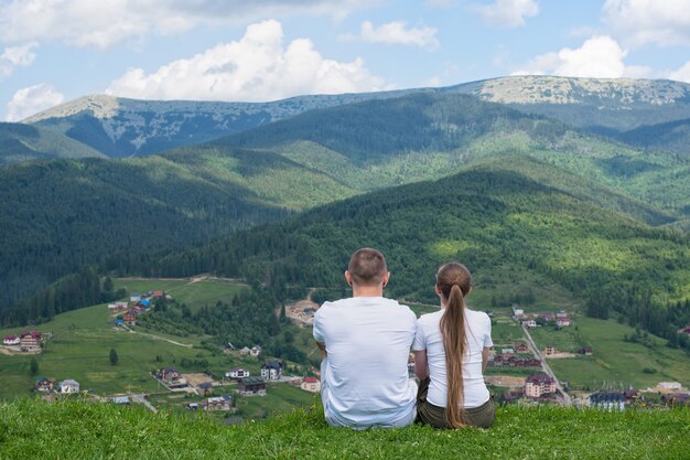 Dois amantes sentam-se em uma colina e admiram a vista das montanhas. Descanse juntos. Vista traseira