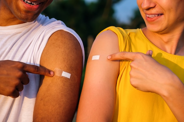 Dois amigos afro-americanos e caucasianos mostrando as mãos após a vacinação