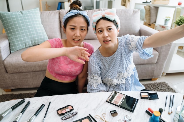 dois amigos blogueiros de linda garota asiática gravando vídeo de beleza juntos antes de começar a mover a câmera da lente. senhora de camisa rosa com gesto com a mão, dizendo o caminho para mudar o ângulo com cosmético na mesa