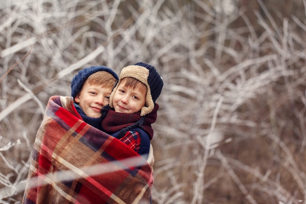 Dois amigos de meninos abraçam sob um cobertor quente na floresta de inverno. . amor de irmão. amizade do conceito