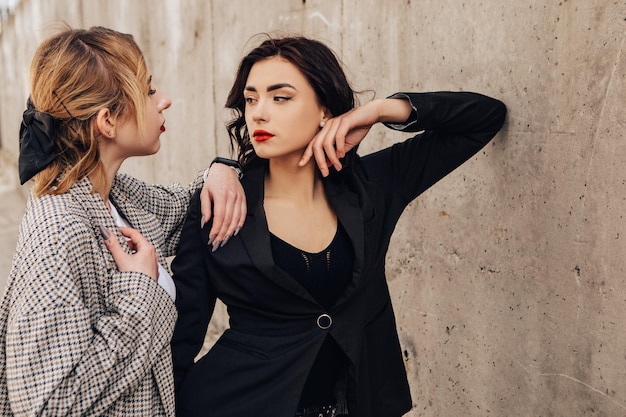 Dois amigos de mulheres bonitas posando perto da parede cinza. Casal de garotas lésbicas gays abraçando abraçando