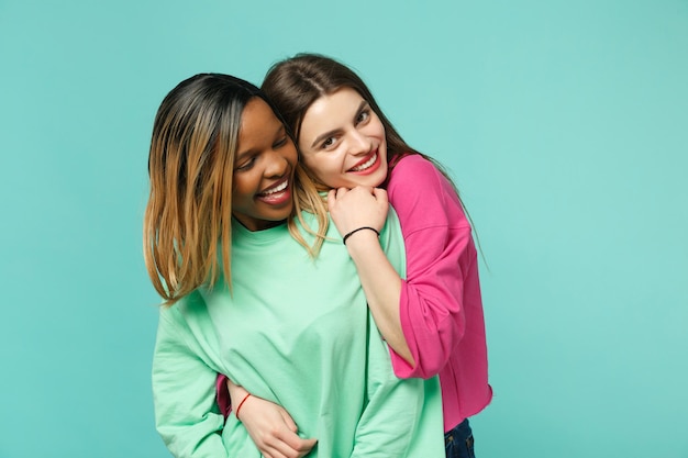 Foto dois amigos de mulheres jovens europeus e afro-americanos em roupas verdes rosa em pé posando isolado no fundo da parede azul turquesa, retrato de estúdio. conceito de estilo de vida de pessoas. mock up espaço de cópia.