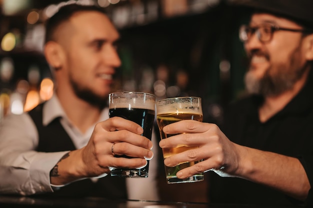 Dois amigos do sexo masculino felizes e sorridentes brindam com copos de chope no balcão do bar