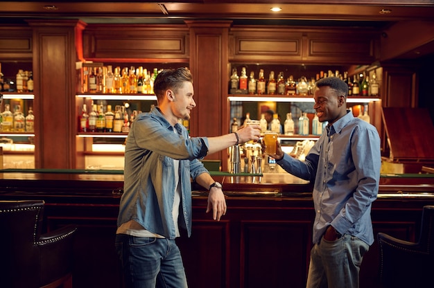 Dois amigos do sexo masculino posam com copos de cerveja no balcão do bar. pessoas relaxam em pubs, estilo de vida noturno, amizade, celebração de eventos