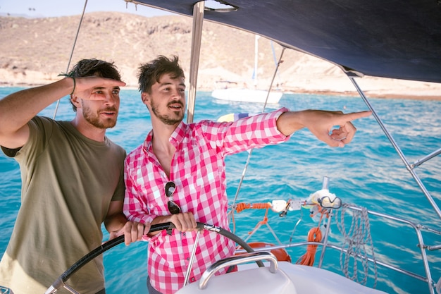 Foto dois amigos enquanto dirigia um barco, um menino aponta com a mão para a frente para mostrar algo ao amigo