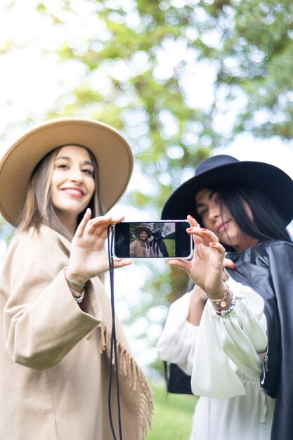 Dois amigos estilosos, ambos pegando um celular para tirar uma selfie