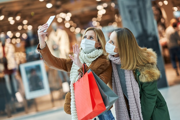 dois amigos fazendo compras juntos usando smartphone e usando uma máscara