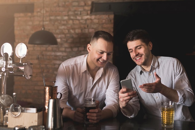 Dois amigos felizes tomando cerveja fresca no bar e navegando nas redes sociais no celular. tecnologias, comunicação online e dependência de internet, espaço de cópia