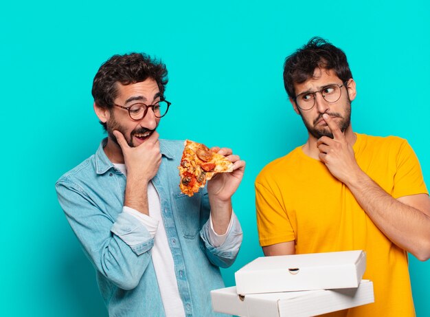 Dois amigos hispânicos pensando em expressão e segurando pizzas para levar