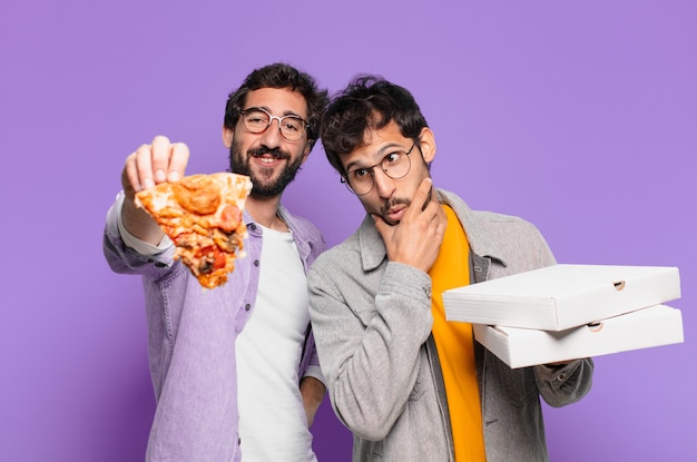 Dois amigos hispânicos pensando em expressão e segurando pizzas para levar