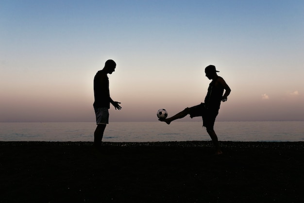 Dois amigos jogando futebol na praia.