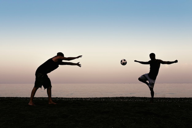 Dois amigos jogando futebol na praia.