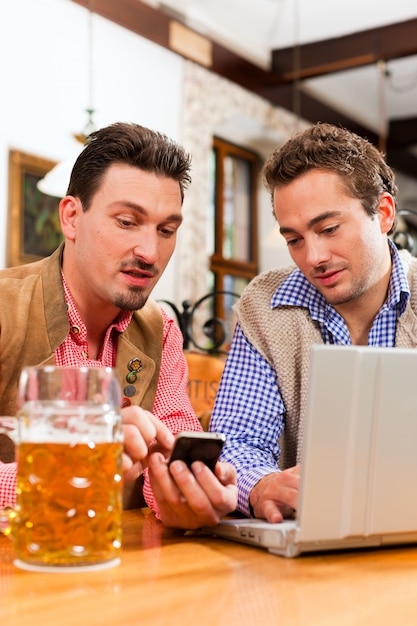 Dois amigos no pub da Baviera com laptop