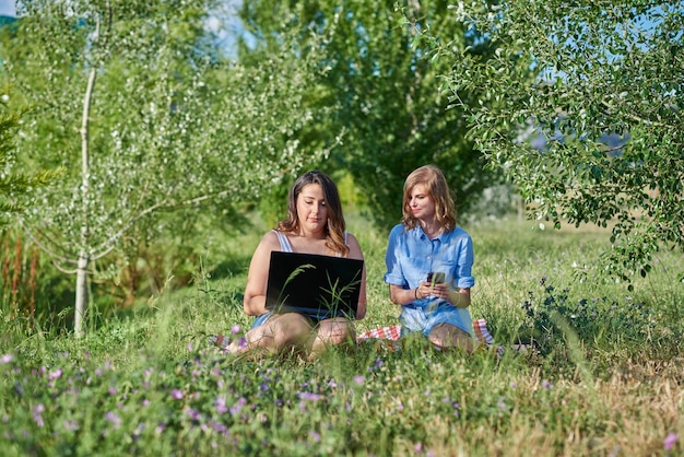 Dois amigos sentados em um parque com um laptop.