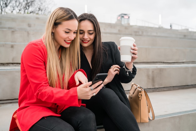 Dois amigos usando seu telefone celular enquanto está sentado ao ar livre.