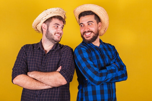 Dois amigos vestindo roupas típicas para a festa junina festa de arraia de são joão com os braços cruzados sorrindo