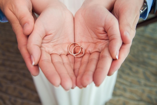 Dois anéis de casamento dourados nas palmas das mãos da noiva e do noivo.