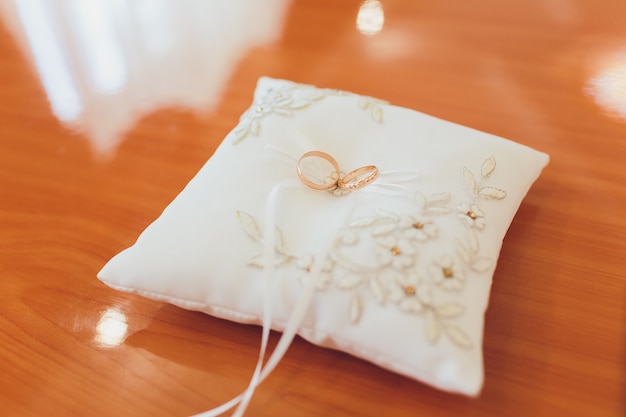 Dois anéis de casamento ouro deitado na almofada de renda de seda para anéis. Os acessórios do casamento noivos antes da cerimônia fotografaram em um fundo branco. anéis no aniversário de casamento.