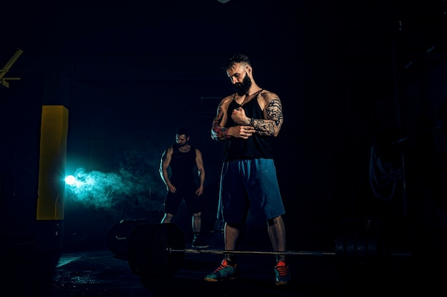 Dois atletas musculosos e tatuados com barbas se preparam para treinar, para levantar a barra de peso