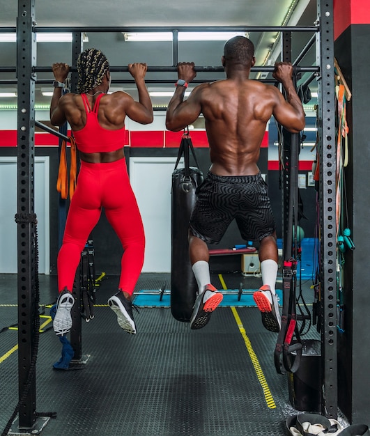Dois atletas negros fisiculturistas em um ginásio de esportes fazendo um exercício com barra para trás. Conceito de fortalecimento do corpo na academia