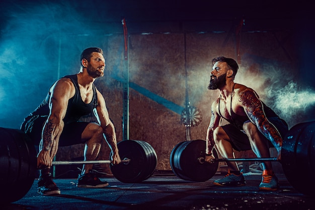 Dois atletas tatuados barbudos musculares treinando na academia