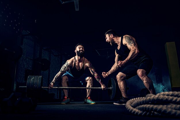 Dois atletas tatuados barbudos musculares treinando na academia