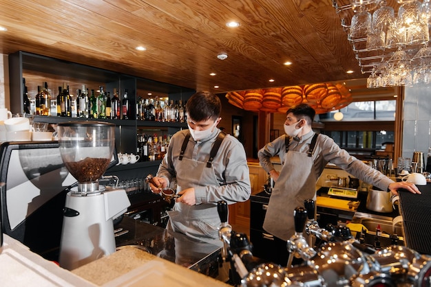 Dois baristas mascarados preparam um delicioso café requintado no bar da cafeteria o trabalho de restaurantes e cafés durante a pandemia