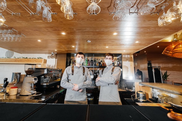 Dois bartenders estilosos de máscaras e uniformes durante a pandemia ficam atrás do bar O trabalho de restaurantes e cafés durante a pandemia