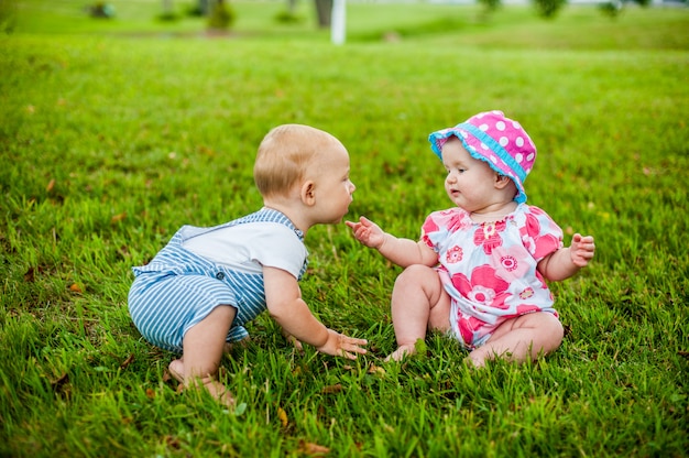 Dois bebê feliz e uma menina com 9 meses de idade, sentados na grama e interagem, conversam, olham um para o outro.