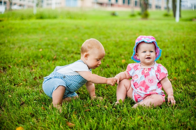 Dois bebê feliz e uma menina com 9 meses de idade, sentados na grama e interagem, conversam, olham um para o outro.