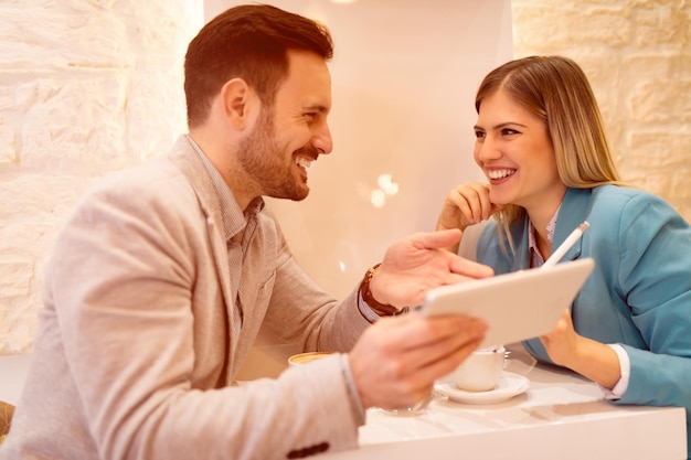 Dois belos jovens sorridentes sentados no café e trabalhando em tablet digital.