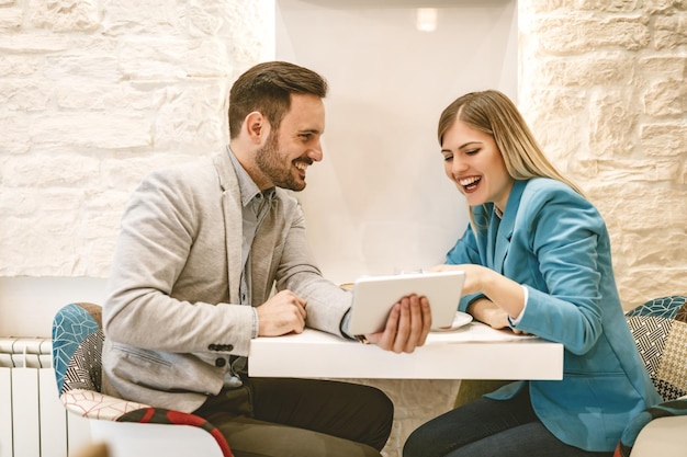 Dois belos jovens sorridentes sentados no café e trabalhando em tablet digital.