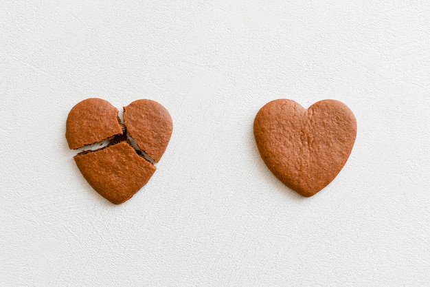 Dois biscoitos em forma de coração, um deles é quebrado em um fundo branco. Quebrar biscoitos em forma de coração como um conceito de romper e terminar relacionamentos, amor não correspondido. Conceito de amor não correspondido .. Valenti